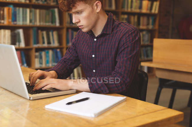 Estudante universitário atento usando laptop na biblioteca — Fotografia de Stock