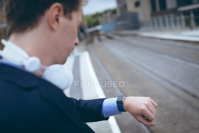 Uomo d'affari che controlla l'ora nel suo smartwatch alla stazione ferroviaria — Foto stock