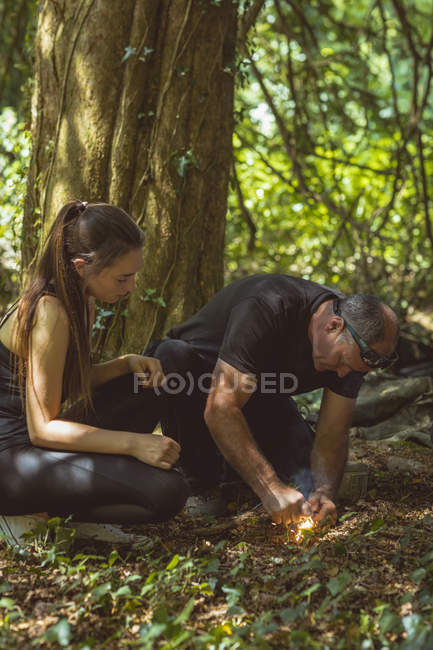 Чоловік і жінка запалюють вогонь у таборі на сонячний день — стокове фото