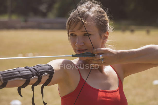 Frau übt sich an sonnigem Tag im Bogenschießen im Bootcamp — Stockfoto