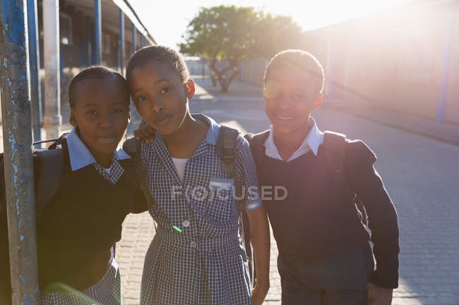 Colegiales de pie en el campus de la escuela en un día soleado - foto de stock