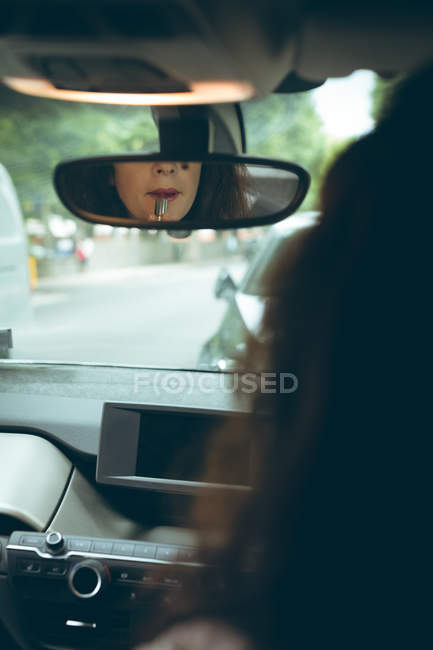 Reflejo de empresaria en espejo aplicando lápiz labial en coche - foto de stock