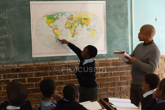 Schoolboy explicando sobre mapa do mundo em sala de aula na escola — Fotografia de Stock
