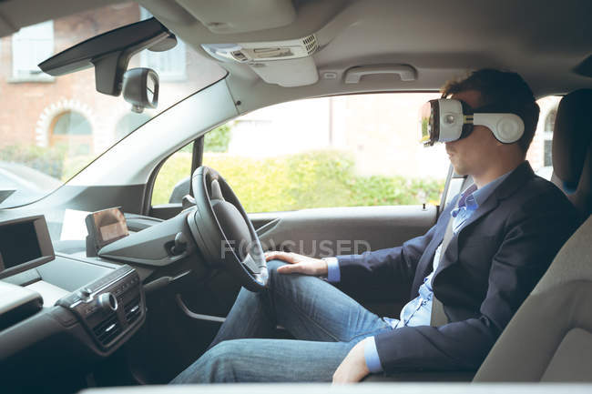 Empresario con auriculares de realidad virtual en un coche - foto de stock