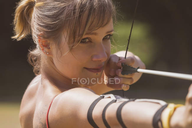 Donna che pratica tiro con l'arco al campo di addestramento in una giornata di sole — Foto stock
