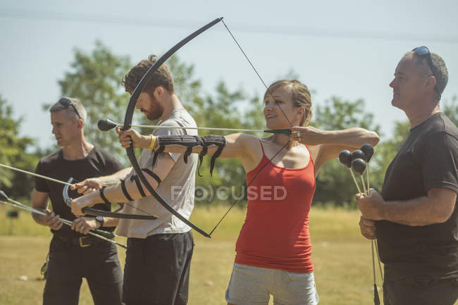 Entrenador instruyendo a la mujer sobre tiro con arco en el campo de entrenamiento - foto de stock