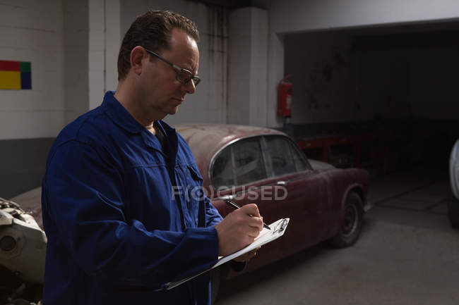 Mechaniker schreibt auf Klemmbrett in Garage — Stockfoto