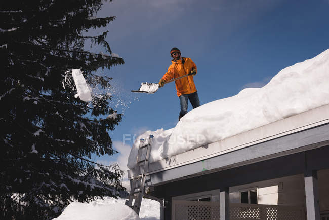 Человек чистит снег с крыши своего магазина зимой — стоковое фото