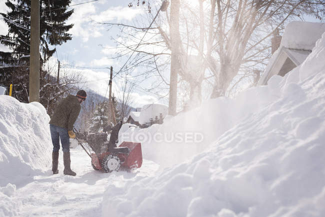 Homme utilisant une machine à souffler la neige dans la région enneigée pendant l'hiver — Photo de stock
