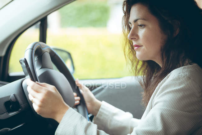 Businesswoman using mobile phone while driving car — Stock Photo