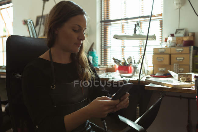 Jewelry designer using mobile phone in workshop — Stock Photo