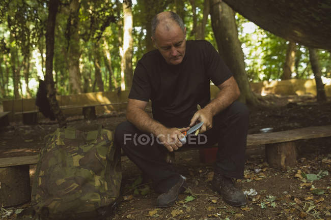 Mature man sharpening stick at boot camp — Stock Photo