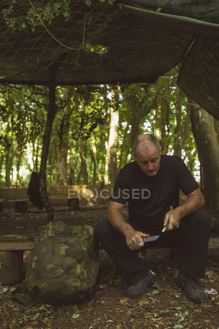 Зрілий чоловік загострює палицю в таборі для завантаження — стокове фото