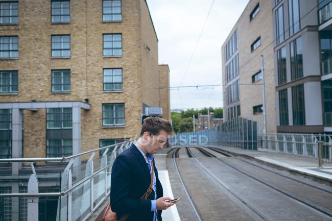 Giovane uomo d'affari che utilizza il telefono cellulare alla stazione ferroviaria — Foto stock