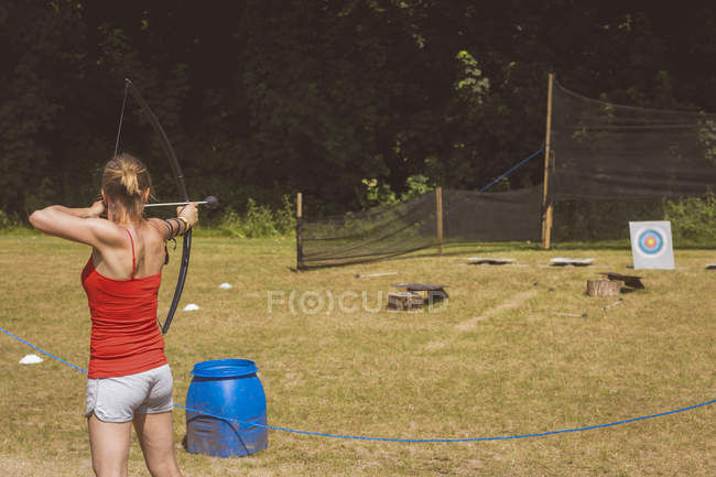 Frau übt sich an sonnigem Tag im Bogenschießen im Bootcamp — Stockfoto