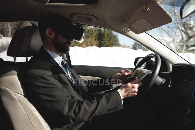 Бизнесмен, использующий гарнитуру виртуальной реальности с цифровым планшетом в автомобиле — стоковое фото
