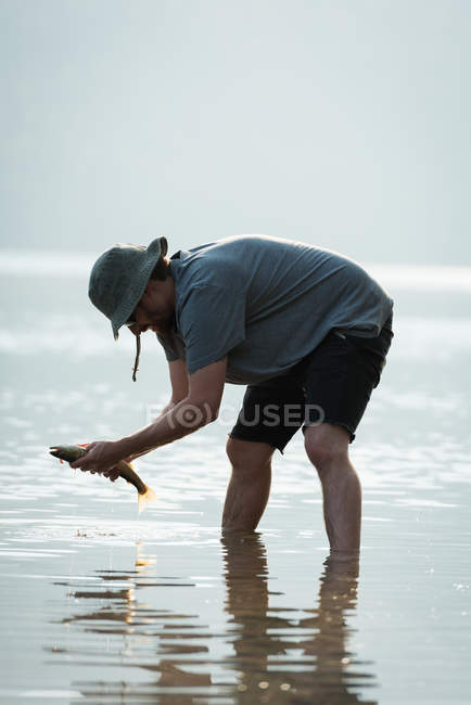 Side view of fisherman holding a fish near riverside — Stock Photo