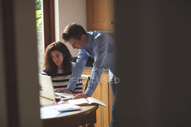 Jeune couple discutant sur ordinateur portable dans la cuisine à la maison — Photo de stock