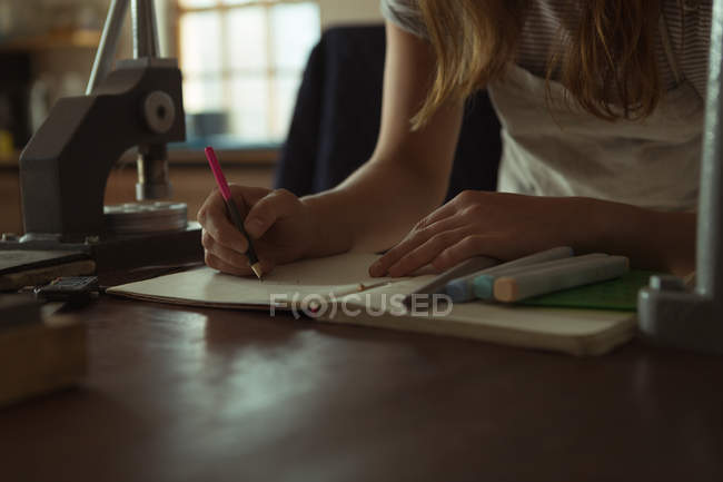 Mid section of jewelry designer writing on a register in workshop — Stock Photo