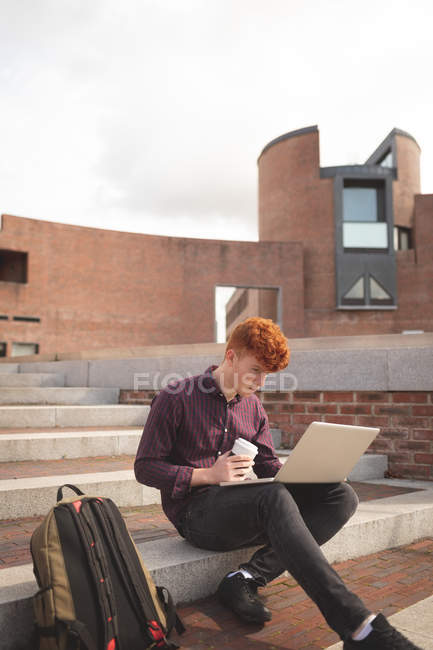 College student using laptop on stairs in college — Stock Photo