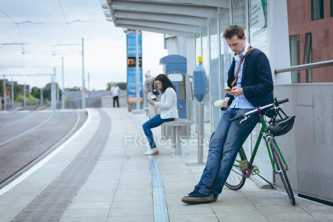 Empresário encostado à bicicleta e usando telefone celular na estação ferroviária — Fotografia de Stock