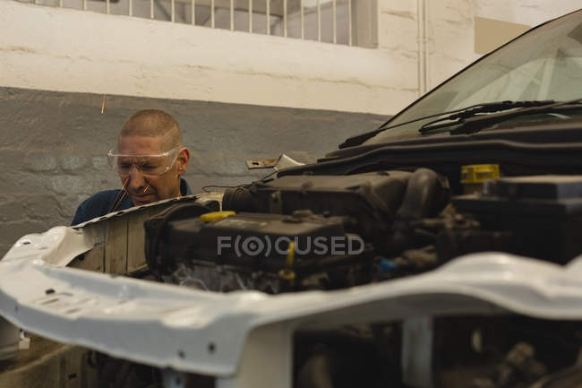 Мужской механик, обслуживающий автомобиль в гараже — стоковое фото