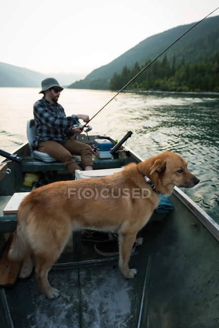 Pescatore pesca con il suo cane nel fiume in campagna — Foto stock