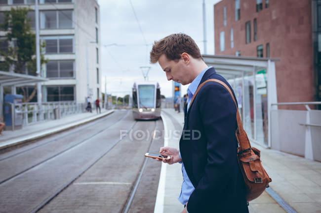 Молодой бизнесмен пользуется мобильным телефоном на вокзале — стоковое фото