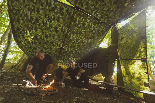 Ajuste hombres encendiendo fuego en el campamento de arranque - foto de stock
