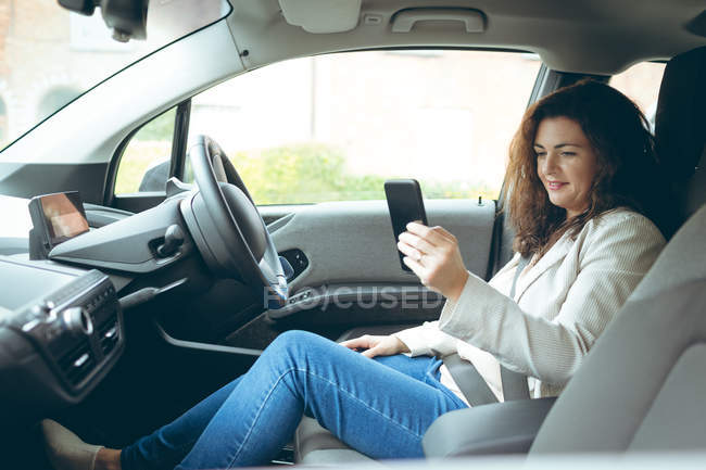 Business woman using mobile phone while driving car — стоковое фото