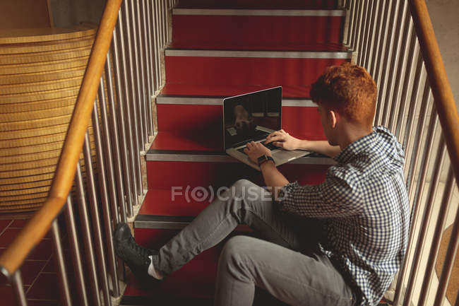 Vista de ángulo alto del estudiante universitario utilizando el ordenador portátil en las escaleras en el campus - foto de stock