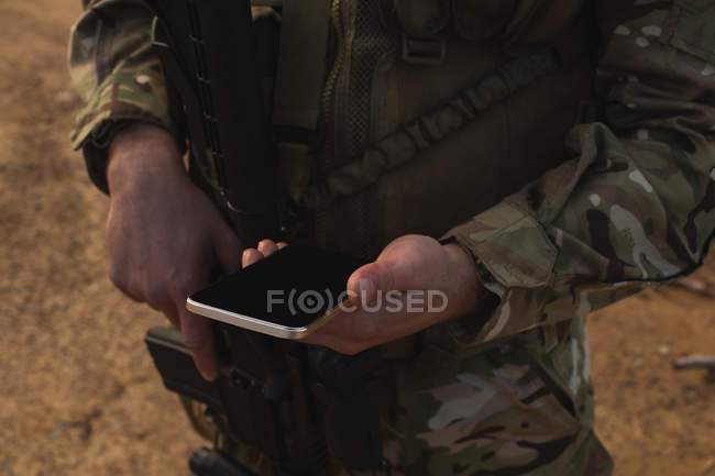 Средняя секция военнослужащего с помощью мобильного телефона во время военной подготовки — стоковое фото
