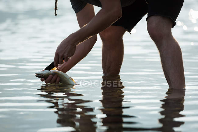 Mid section of fisherman holding a fish near riverside — Stock Photo