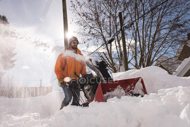 Hombre utilizando la máquina de soplador de nieve en la región nevada durante el invierno - foto de stock