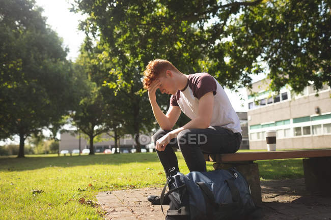 Estudiante universitario preocupado sentado en el campus - foto de stock