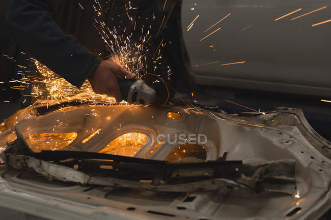 Чоловіча механічна шліфувальна машина на автомобільній частині в гаражі — стокове фото