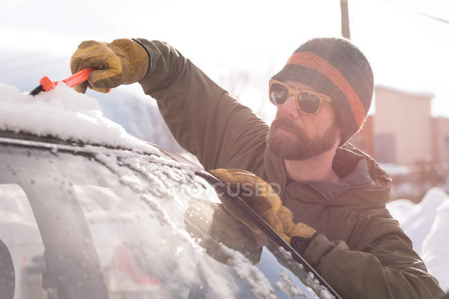 Man cleaning snow from car windshield during winter — Stock Photo