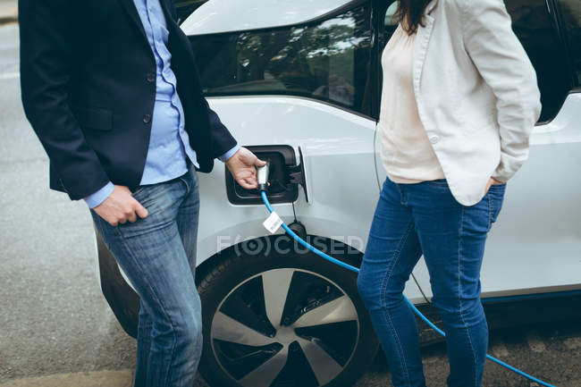 Mid section of business colleagues charging electric car at charging station — Stock Photo