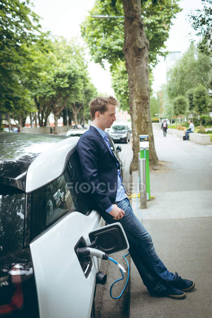 Вдумчивый бизнесмен заряжает электромобиль на зарядной станции — стоковое фото