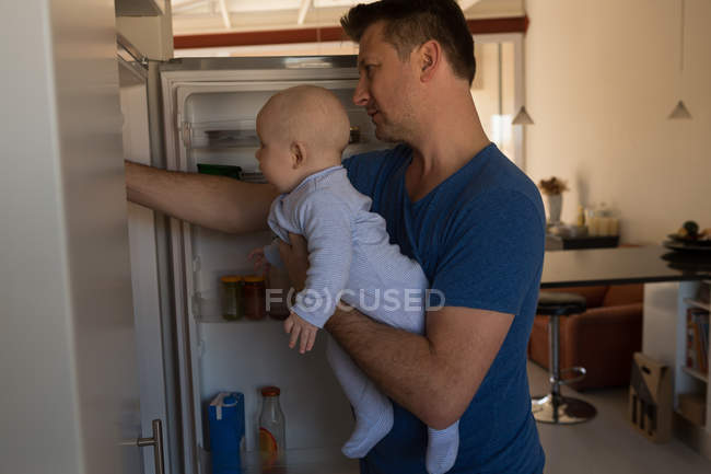 Pai e bebê à procura de comida na geladeira em casa — Fotografia de Stock