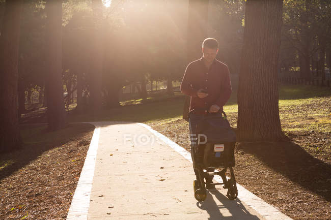 Father using mobile phone with baby boy in pram at park — Stock Photo