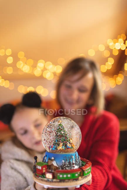 Mother and daughter watching Christmas tree snow globe at home — Stock Photo