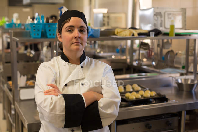 Retrato de una chef de pie con los brazos cruzados en la cocina - foto de stock