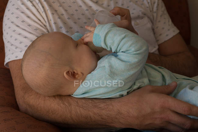 Отец кормит своего малыша молоком в гостиной — стоковое фото