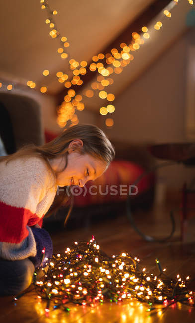 Chica sonriente mirando luces de hadas iluminadas en casa - foto de stock