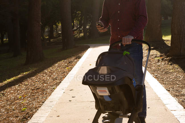 Père utilisant un téléphone portable avec bébé garçon en landau au parc — Photo de stock