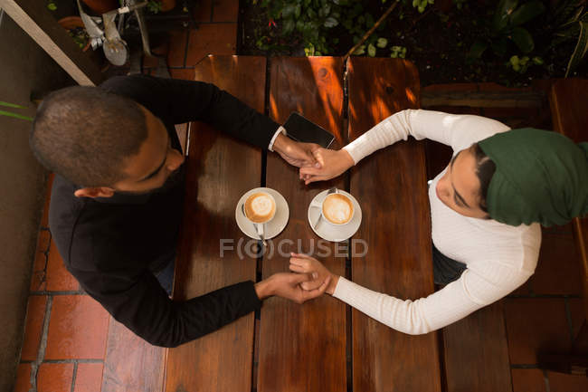 Накладные расходы пары, держащейся за руки в кафе — стоковое фото