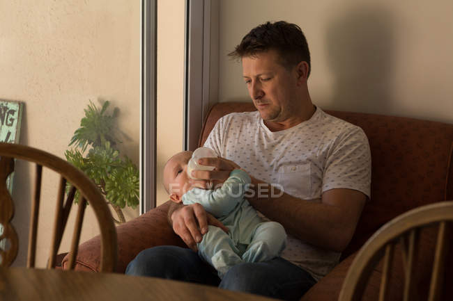 Отец кормит своего малыша молоком в гостиной — стоковое фото