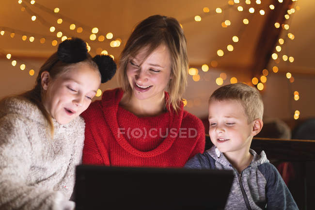 Улыбающаяся мать и дети используют ноутбук дома во время Рождества — стоковое фото