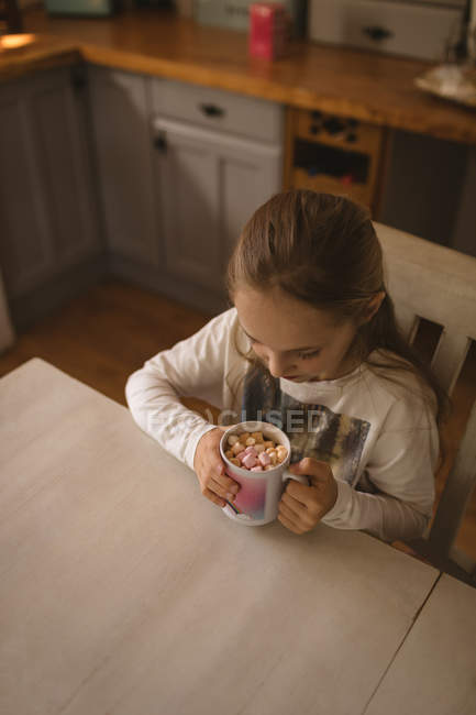 Girl looking at marshmallows in the cup at home — Stock Photo
